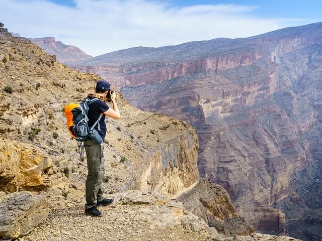 Fotografo con zaino che scatta foto da una rupe rocciosa affacciata su Jebel Shams.