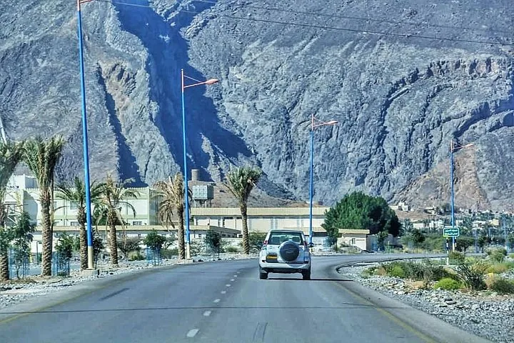 Auto fährt auf einer Straße auf steile, felsige Berge im Jebel Shams zu.
