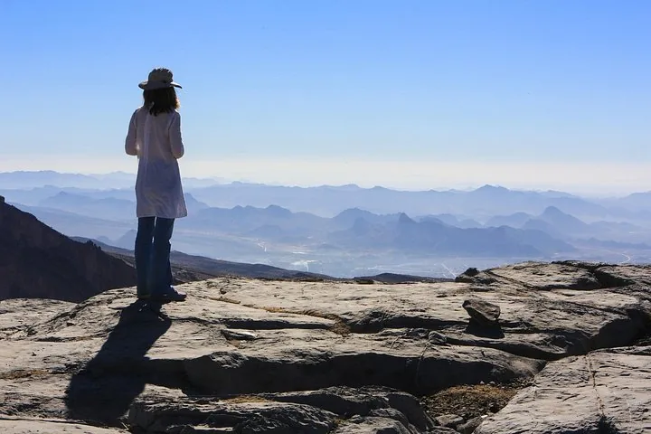 Woman looking at hazy mountain ranges from Jebel Shams viewpoint.