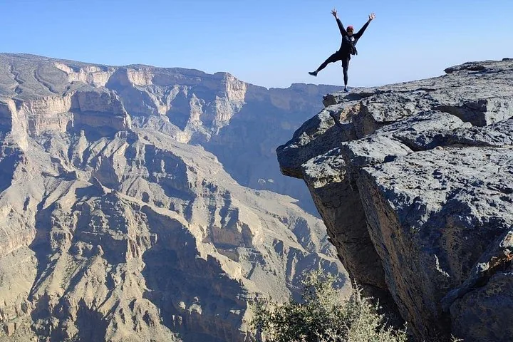 Personne en équilibre sur une jambe au bord d'un rocher surplombant un canyon profond.